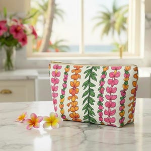 May include: A white cosmetic bag with a floral pattern in pink, orange, and green. The bag has a gold zipper and is sitting on a marble surface. Several flowers are in front of the bag.