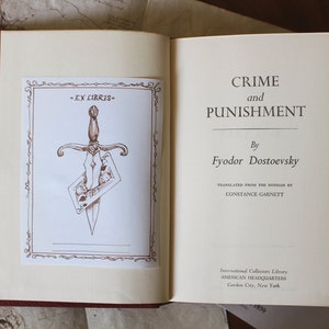 Puede incluir: Un libro vintage titulado "Crimen y Castigo" de Fi&oacute;dor Dostoievski. La portada del libro presenta una ilustraci&oacute;n marr&oacute;n de una daga que atraviesa una carta de juego. El libro forma parte de la International Collectors Library, American Headquarters, Garden City, New York.