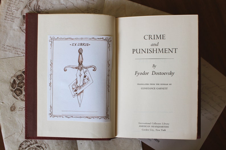 Puede incluir: Un libro vintage titulado "Crimen y Castigo" de Fi&oacute;dor Dostoievski. La portada del libro presenta una ilustraci&oacute;n marr&oacute;n de una daga que atraviesa una carta de juego. El libro forma parte de la International Collectors Library, American Headquarters, Garden City, New York.