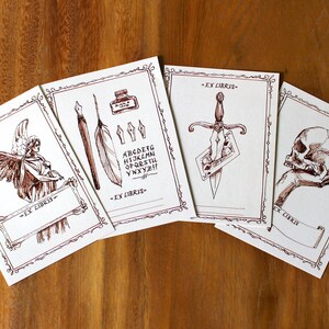 Puede incluir: Cuatro ex libris marrones y blancos con bordes decorativos. Cada ex libris presenta una imagen diferente: un &aacute;ngel, una pluma y un tintero, una daga y una calavera. Cada ex libris incluye el texto "Ex Libris".