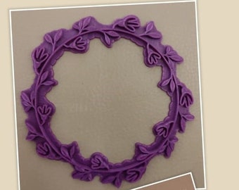 May include: A purple rubber stamp with a floral wreath design. The stamp is used to create an impression on paper or cardstock.