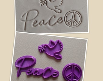 May include: Two sets of cookie cutters, one in gray and one in purple, featuring a dove with an olive branch, the word "Peace" in a cursive font, and a peace sign.