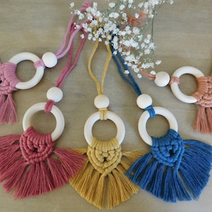 Peut inclure: Cinq ornements en bois avec anneau et pompon dans les tons rose, rouge, jaune, bleu et marron. Les anneaux sont enfilés sur des cordons avec des perles en bois.
