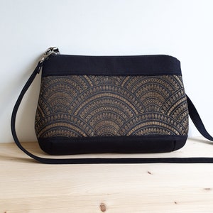 Un sac bandoulière bi-matière. Une bande noire en haut et en bas faites dans un solide sergé de coton. Au milieu un tissu jacquard bronze et noir, aux motifs éventails, légèrement brillant.