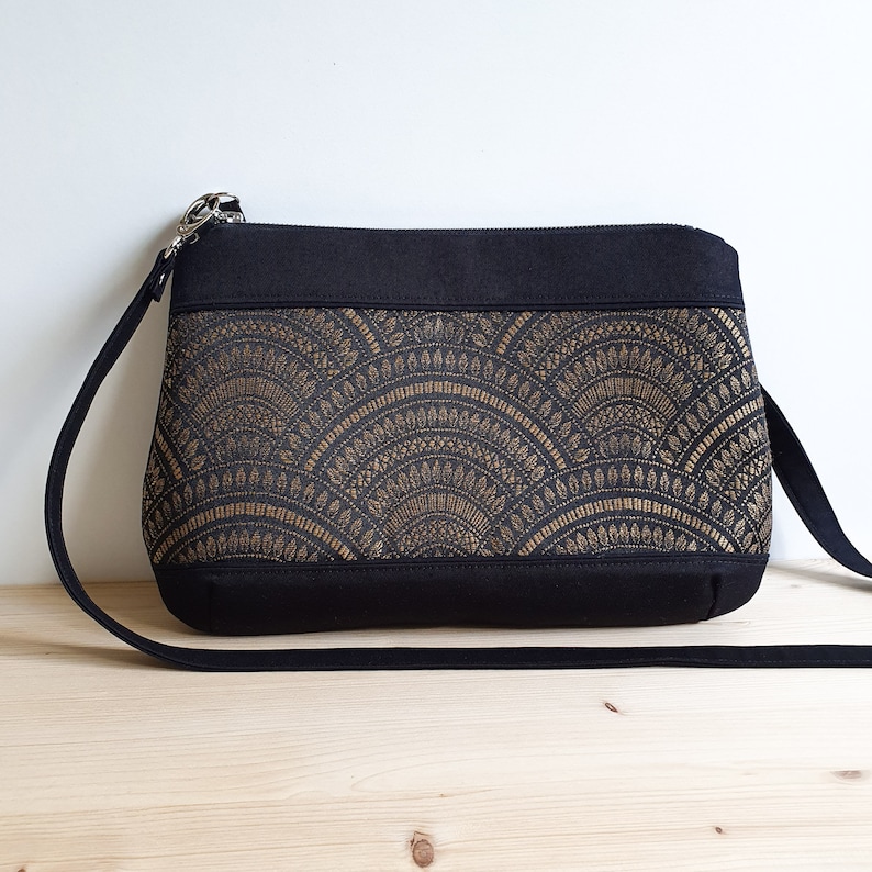 Un sac bandoulière bi-matière. Une bande noire en haut et en bas faites dans un solide sergé de coton. Au milieu un tissu jacquard bronze et noir, aux motifs éventails, légèrement brillant.