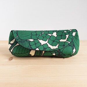 May include: A rectangular fabric case with a rounded flap closure, featuring a repeating pattern of green hydrangea-like flowers and dark green leaves on a cream-colored background. The case has a structured shape and a textured textile finish.