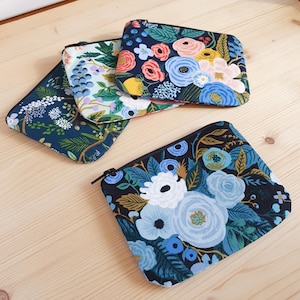 Puede incluir: Cuatro estuches con cremallera con estampado floral en tonos azules, rosas y amarillos. Los estuches son rectangulares con esquinas redondeadas y cremalleras negras. Los estampados florales incluyen rosas, peonías y otras flores.