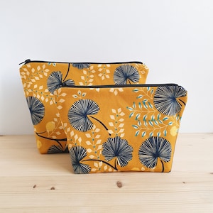 May include: Two yellow fabric zippered pouches with a black trim and a blue and yellow floral pattern. The smaller pouch is in front of the larger pouch.