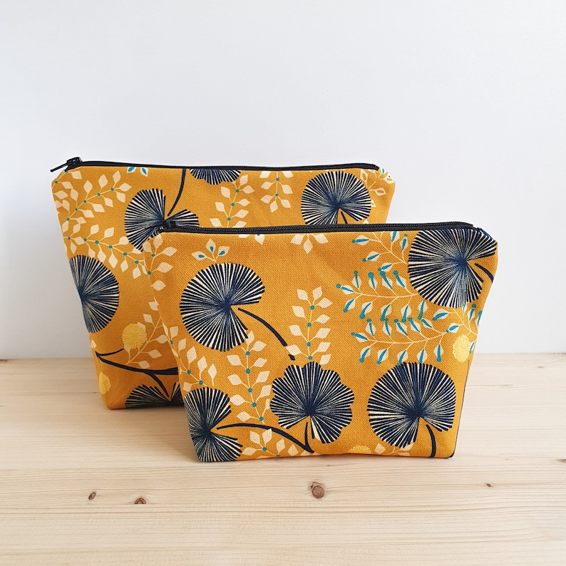 May include: Two yellow fabric zippered pouches with a black trim and a blue and yellow floral pattern. The smaller pouch is in front of the larger pouch.