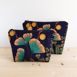May include: Two zippered pouches with a navy blue background and a floral print featuring yellow, green, and orange ginkgo leaves and berries.