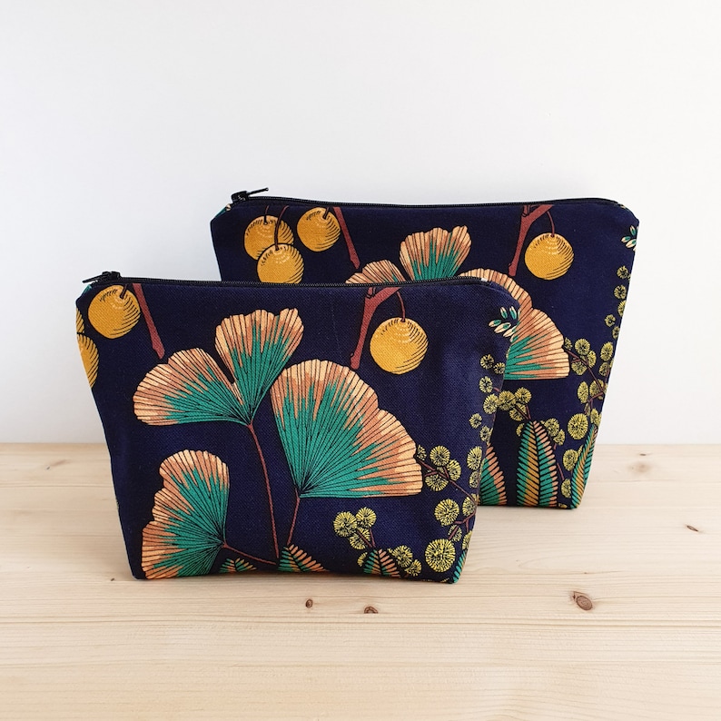 May include: Two zippered pouches with a navy blue background and a floral print featuring yellow, green, and orange ginkgo leaves and berries.