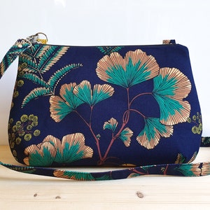 Un sac à main posé sur une table de bois clair. De forme légèrement arrondie, il est orné de motifs de ginkgo, feuilles et mimosa.