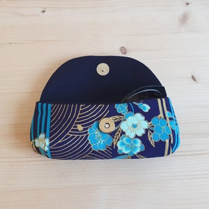 May include: A blue and gold floral patterned glasses case with a black lining and a gold snap closure.
