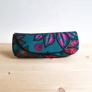 May include: A rectangular fabric pouch featuring a teal background with a repeating pattern of stylized leaves in shades of magenta, orange, and dark blue. The pouch has a curved flap closure that extends across the front of the item.