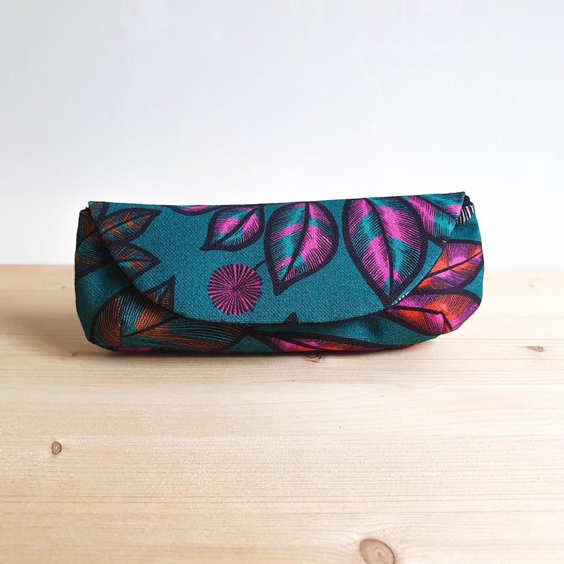 May include: A rectangular fabric pouch featuring a teal background with a repeating pattern of stylized leaves in shades of magenta, orange, and dark blue. The pouch has a curved flap closure that extends across the front of the item.