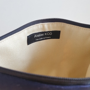 May include: The inside of a black zippered pouch with a cream colored lining. A black label with white text reads "Atelier KOD Fait main en France".