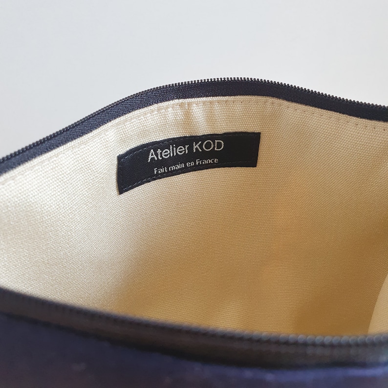 May include: The inside of a black zippered pouch with a cream colored lining. A black label with white text reads "Atelier KOD Fait main en France".