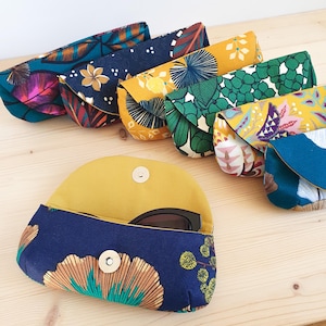 May include: A collection of six fabric eyeglass cases featuring various floral and botanical patterns in colors including navy blue, mustard yellow, teal, and green. Each case has a curved flap with a silver magnetic snap closure.
