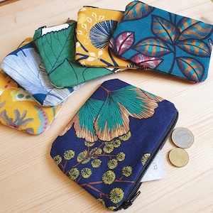 Puede incluir: Una colección de monederos rectangulares con diseños florales y de hojas coloridos. Los monederos presentan colores como el verde azulado, amarillo, verde y azul. Cada monedero tiene una cremallera negra. Algunos monederos contienen monedas.