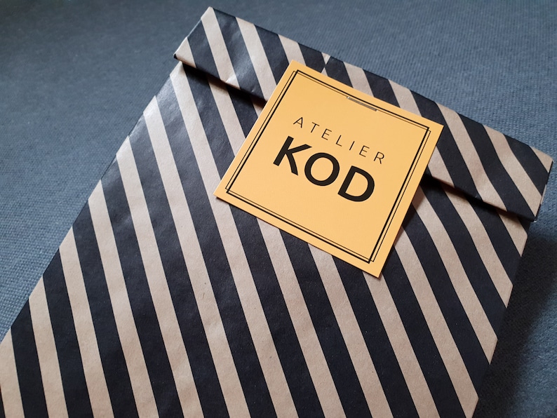 May include: A brown paper bag with black stripes and a yellow square label that says "Atelier Kod".