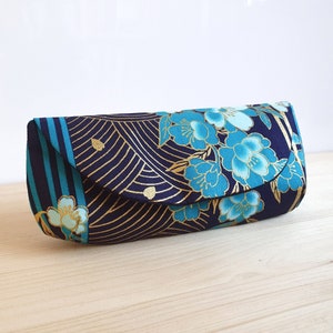 May include: A blue and gold fabric eyeglass case with a floral pattern. The case has a flap that closes with a snap.