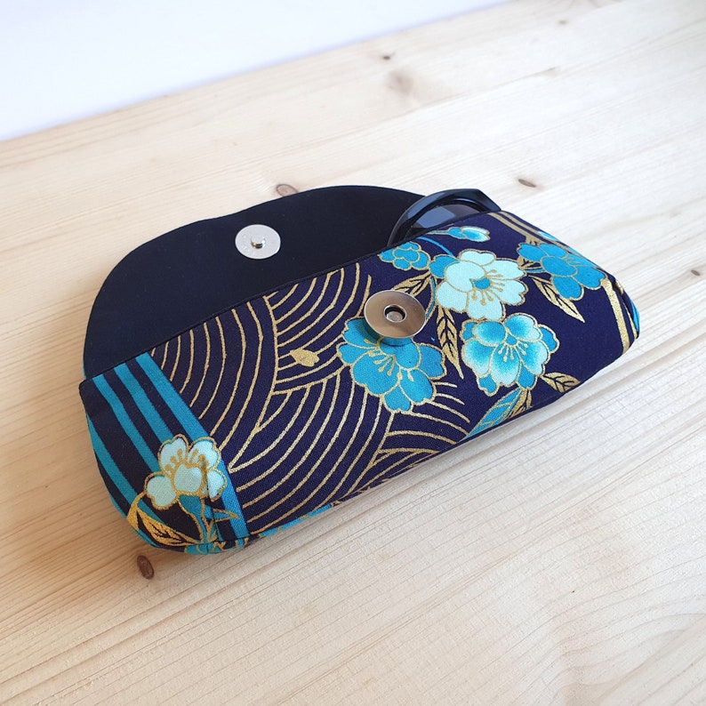 May include: A black and blue fabric eyeglasses case with a floral pattern and a gold snap closure.