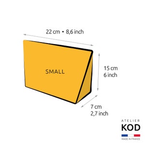以下が含まれることがあります： 「SMALL」とラベル付けされた黄色い三角形のクッションで、インチとセンチメートルで寸法が示されています。クッションの幅は8.6インチ、高さは6インチ、深さは2.7インチです。