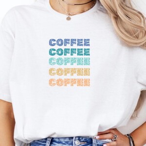 May include: White t-shirt with the word "COFFEE" repeated five times in a gradient of blue, teal, green, yellow, and orange.