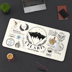 May include: A white mousepad with a black and white design featuring a mountain range, stars, and the words "VELARIS City of Starlight". There are other black and white illustrations around the border, including a sword, a crescent moon, and a book.