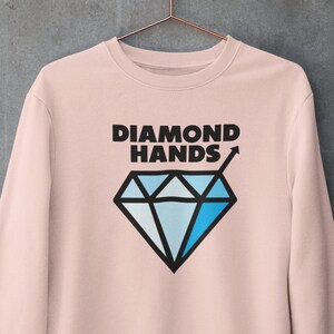 Könnte beinhalten: Ein rosa Sweatshirt mit einer schwarzen Diamantgrafik und dem Text "DIAMOND HANDS" mit einem nach oben zeigenden Pfeil.