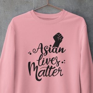 May include: A pink sweatshirt with the text "Asian lives matter" in black lettering and a black fist raised in the air.