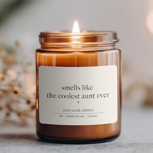 May include: A lit candle in a clear glass jar with a metal lid. The label reads "smells like the coolest aunt ever" with "aunt sarah edition" below. The candle is 9 oz and made of natural soy wax, with a burn time of 50 hours.
