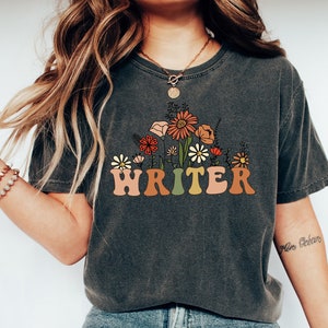 May include: A dark gray t-shirt with a floral design and the word "WRITER" in colorful letters.