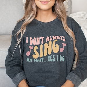 May include: A dark gray sweatshirt with the text "I don't always sing... oh wait... yes I do" in colorful retro font with musical notes.