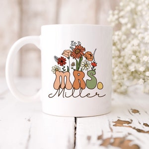 May include: White ceramic mug with a floral design and the text "MRS. Miller" in a retro font.