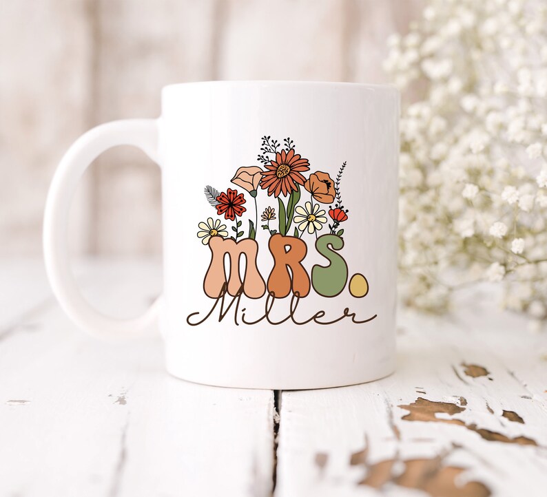 May include: White ceramic mug with a floral design and the text "MRS. Miller" in a retro font.