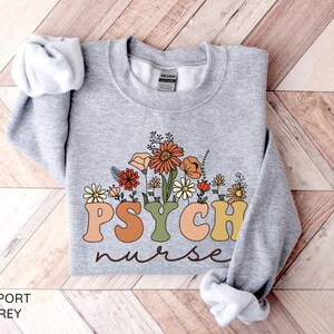 May include: A gray sweatshirt with the text "PSYCH nurse" in colorful letters with a floral design behind the text.