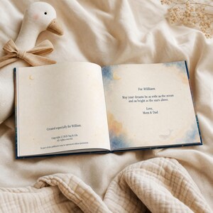 May include: An open hardcover book with cream-colored pages featuring blue and orange watercolor accents. The text reads: For William, May your dreams be as wide as the ocean and as bright as the stars above. Love, Mom & Dad. Created especially for William.