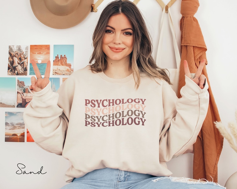 May include: A beige sweatshirt with the word "Psychology" repeated four times in a retro font. The text is in shades of pink and brown.