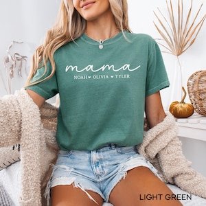 May include: Light green t-shirt with the word "mama" in white script, followed by the names Noah, Olivia, and Tyler. The shirt is a crew neck and is worn with denim shorts. The words "LIGHT GREEN" are at the bottom of the image.