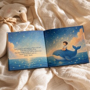 May include: An open children's storybook featuring an illustration of a child sitting on a blue whale in a starry ocean. The text reads: Soon, William was resting on Mara's soft back, as if it were a floating cloud. The whale began to hum, and the whole ocean seemed to breathe in and out... slowly... slowly.