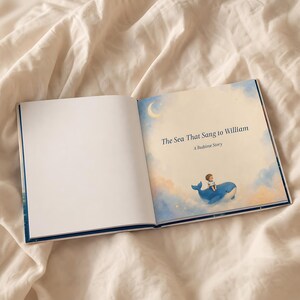 May include: An open hardcover book titled The Sea That Sang to William: A Bedtime Story. The right page features a soft-toned illustration of a small child riding a blue whale amidst clouds and a crescent moon against a pale yellow sky.