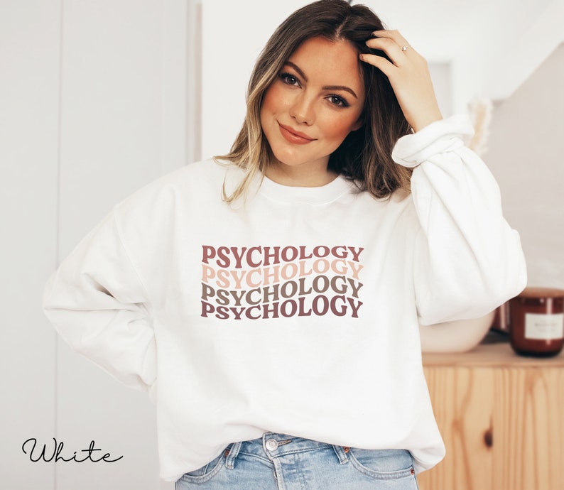 May include: White sweatshirt with the word "Psychology" repeated four times in a stacked, retro-style font. The text is in shades of pink and brown.