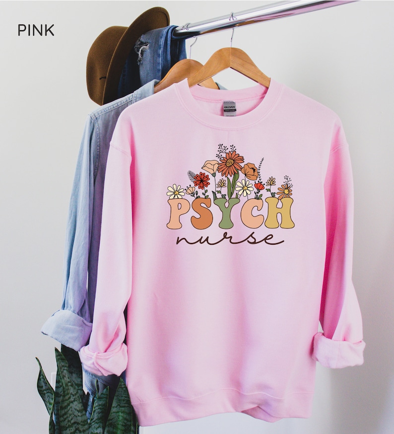 May include: Pink sweatshirt with a floral design and the text "PSYCH nurse" in a retro font.
