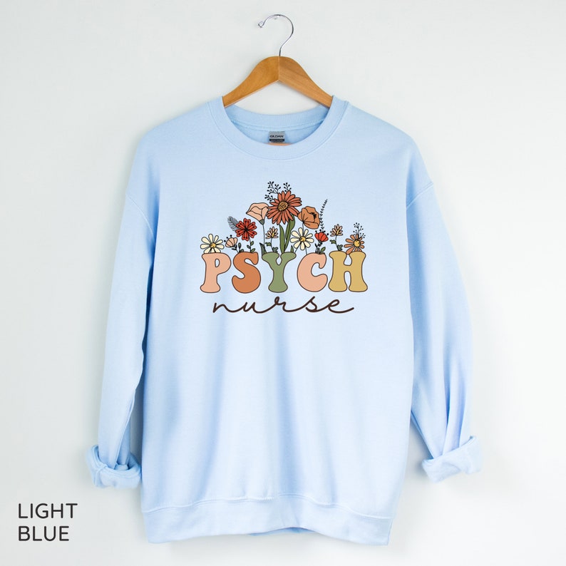 May include: Light blue sweatshirt with a floral design and the text "PSYCH nurse" in colorful letters.