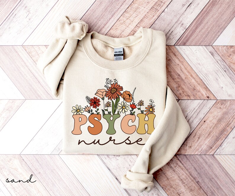May include: A cream-colored sweatshirt with a floral design and the text "PSYCH nurse" in colorful, retro-style lettering.