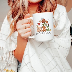 May include: White ceramic mug with a floral design and the text "MRS. Miller" in brown, green, and orange lettering.