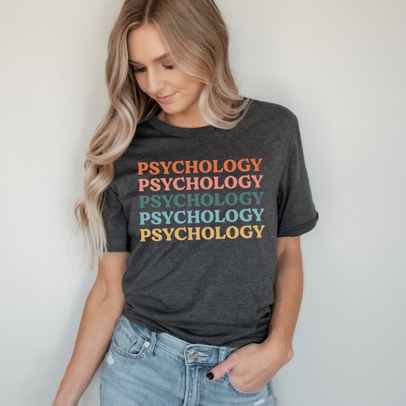 May include: A dark heather grey t-shirt with the word "Psychology" repeated five times in a rainbow color scheme. The text is stacked vertically, with each word in a different color: orange, pink, blue, teal, and yellow.