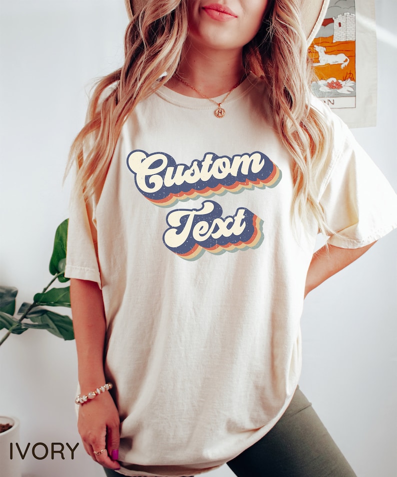 May include: A white t-shirt with a retro-style graphic that says "Custom Text" in a rainbow of colors. The shirt is made of a soft, comfortable material and is perfect for everyday wear.