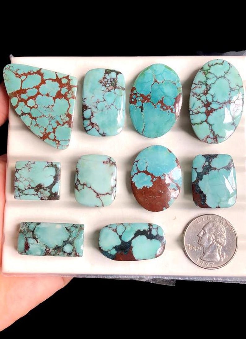 May include: A collection of turquoise gemstones in various shapes, including oval, rectangular, and freeform. The stones display a vibrant blue-green color with brown matrix patterns. A US quarter is included for size reference.